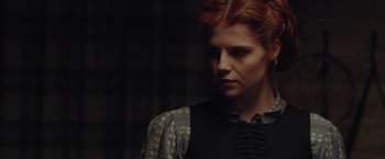 Movie still from “Apostle” (2018), directed by Gareth Evans – A woman with red curly hair wearing a black shirt; Close Up shot, Over the shoulder angle