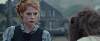 Movie still from “Apostle” (2018), directed by Gareth Evans – A woman with red curly hair and a blue vest; Close Up shot, Over the shoulder angle