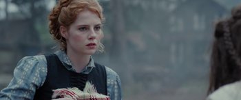 Movie still from “Apostle” (2018), directed by Gareth Evans – A woman with red curly hair holding a book; Close Up shot, Over the shoulder angle