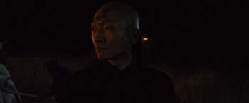 Movie still from “Apostle” (2018), directed by Gareth Evans – A man in a black shirt is in the dark; Close Up shot, Over the shoulder angle