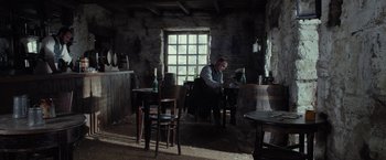 Movie still from “Apostle” (2018), directed by Gareth Evans – A man sitting at a table in front of a window; Wide shot, High angle