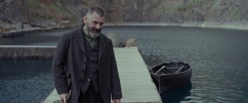Movie still from “Apostle” (2018), directed by Gareth Evans – An old man standing next to a body of water; Medium shot, Over the shoulder angle