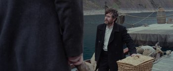 Movie still from “Apostle” (2018), directed by Gareth Evans – A man standing next to a body of water; Medium shot, Over the shoulder angle