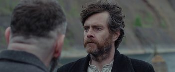 Movie still from “Apostle” (2018), directed by Gareth Evans – A man with a beard is talking to another man; Close Up shot, Over the shoulder angle