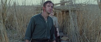 Movie still from “Apostle” (2018), directed by Gareth Evans – A man and a woman standing next to each other in a field; Medium shot, Low angle