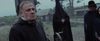 Movie still from “Apostle” (2018), directed by Gareth Evans – A man and a woman dressed in black standing next to each other in a field; Medium shot, Over the shoulder angle