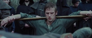 Movie still from “Apostle” (2018), directed by Gareth Evans – A man holding a wooden stick in his hand; Medium shot, Over the shoulder angle