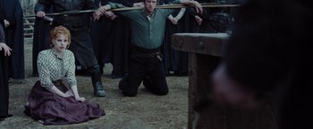 Movie still from “Apostle” (2018), directed by Gareth Evans – A man kneeling on the ground holding a wooden stick; Medium shot, Over the shoulder angle