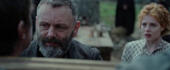 Movie still from “Apostle” (2018), directed by Gareth Evans – A man with a gray beard sitting in front of a wooden table; Close Up shot, Over the shoulder angle