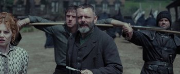 Movie still from “Apostle” (2018), directed by Gareth Evans – A man with a beard holding a knife in front of another man with a beard; Medium shot, Over the shoulder angle