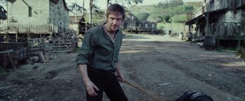 Movie still from “Apostle” (2018), directed by Gareth Evans – A man holding a wooden stick on a dirt field; Medium shot, Over the shoulder angle