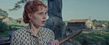 Movie still from “Apostle” (2018), directed by Gareth Evans – A woman holding a wooden stick in her hand; Close Up shot, Low angle