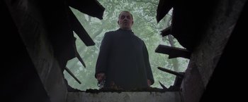 Movie still from “Apostle” (2018), directed by Gareth Evans – A man standing in the middle of a forest; Medium shot, Low angle