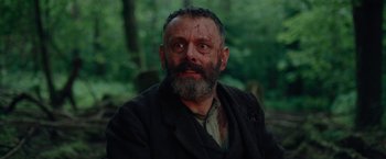 Movie still from “Apostle” (2018), directed by Gareth Evans – A person wearing a suit and a beard; Close Up shot, Low angle