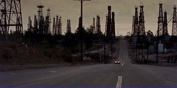 Movie still from “Written on the Wind” (1956), directed by Douglas Sirk – An empty road with oil rigs in the background; Extreme Wide shot, High angle