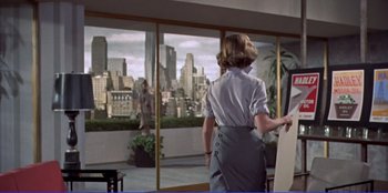 Movie still from “Written on the Wind” (1956), directed by Douglas Sirk – A woman standing in front of a window with a view of a city; Wide shot, Low angle