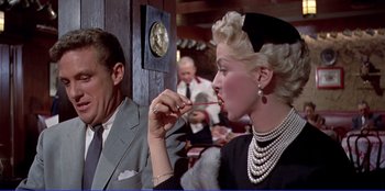 Movie still from “Written on the Wind” (1956), directed by Douglas Sirk – A woman in a black dress is eating a lollipop; Medium shot, Over the shoulder angle