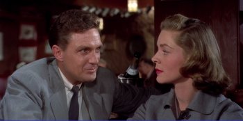 Movie still from “Written on the Wind” (1956), directed by Douglas Sirk – A man and a woman sitting at a table in front of a bottle; Close Up shot, Low angle