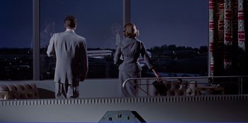 Movie still from “Written on the Wind” (1956), directed by Douglas Sirk – A man and a woman looking out of a window at an airport; Wide shot, Low angle