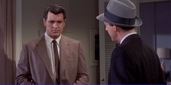 Movie still from “Written on the Wind” (1956), directed by Douglas Sirk – A man in a suit and a hat talking to another man in a suit and a hat; Medium shot, Over the shoulder angle