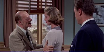 Movie still from “Written on the Wind” (1956), directed by Douglas Sirk – A man and a woman standing next to each other in front of another man; Medium shot, Over the shoulder angle