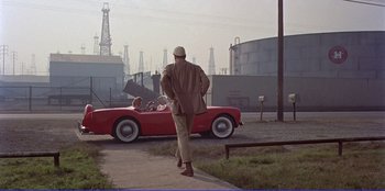 Movie still from “Written on the Wind” (1956), directed by Douglas Sirk – A man walking down the street in front of a red car; Wide shot, Over the shoulder angle