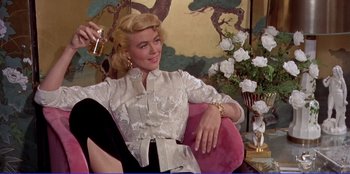 Movie still from “Written on the Wind” (1956), directed by Douglas Sirk – A woman sitting in a chair holding a drink; Medium shot, Low angle