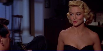 Movie still from “Written on the Wind” (1956), directed by Douglas Sirk – A woman in a black dress sitting on a couch; Medium shot, Over the shoulder angle