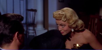 Movie still from “Written on the Wind” (1956), directed by Douglas Sirk – A woman in a black dress with a bow in her hair; Close Up shot, Over the shoulder angle
