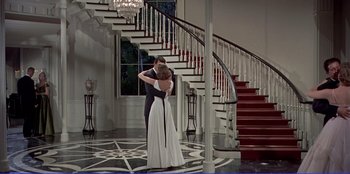 Movie still from “Written on the Wind” (1956), directed by Douglas Sirk – A man and a woman hugging in front of a staircase; Wide shot, High angle