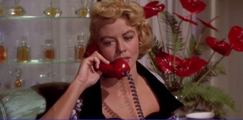 Movie still from “Written on the Wind” (1956), directed by Douglas Sirk – A woman talking on a red phone while sitting in a chair; Close Up shot, Low angle