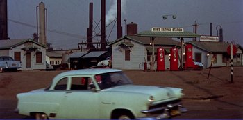 Movie still from “Written on the Wind” (1956), directed by Douglas Sirk – An old car parked in front of a gas station; Wide shot, Low angle