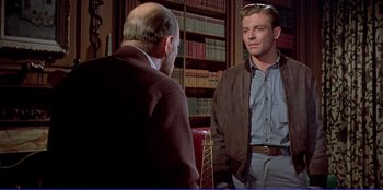 Movie still from “Written on the Wind” (1956), directed by Douglas Sirk – A man standing next to another man in front of a book shelf; Medium shot, Over the shoulder angle