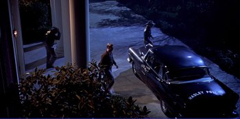 Movie still from “Written on the Wind” (1956), directed by Douglas Sirk – Two men standing next to an old car on the sidewalk; Extreme Wide shot, High angle