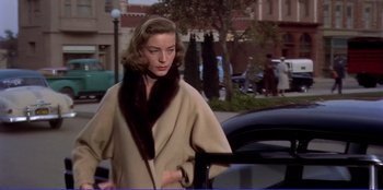Movie still from “Written on the Wind” (1956), directed by Douglas Sirk – A woman walking down a street next to a black car; Medium shot, Low angle