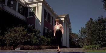 Movie still from “Written on the Wind” (1956), directed by Douglas Sirk – A woman walking in front of a large white building; Wide shot, Low angle