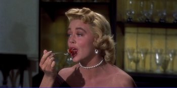 Movie still from “Written on the Wind” (1956), directed by Douglas Sirk – A woman in a black dress is eating a piece of food; Close Up shot, High angle
