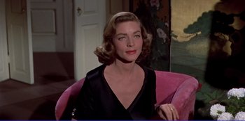 Movie still from “Written on the Wind” (1956), directed by Douglas Sirk – A woman sitting on a pink chair wearing a black dress; Medium shot, Over the shoulder angle