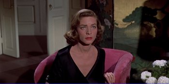 Movie still from “Written on the Wind” (1956), directed by Douglas Sirk – A woman sitting on a pink chair in a room; Close Up shot, High angle