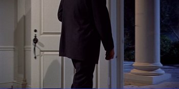 Movie still from “Written on the Wind” (1956), directed by Douglas Sirk – A man in a black suit walking in front of a white door; Medium shot, High angle