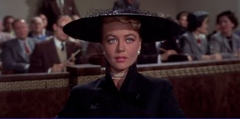 Movie still from “Written on the Wind” (1956), directed by Douglas Sirk – A woman in a black coat and a black hat; Close Up shot, Over the shoulder angle