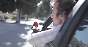 Movie still from “Wrong” (2012), directed by Quentin Dupieux – A man driving a car holding a steering wheel; Close Up shot, Low angle