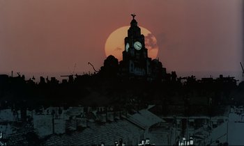 Movie still from “Yellow Submarine” (1968), directed by George Dunning – The sun sets behind a building with a clock on it; Extreme Wide shot, Low angle