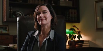 Movie still from “Yellowstone” (2018), created by John Linson – A woman sitting in an office chair smiling for the camera; Close Up shot, Low angle