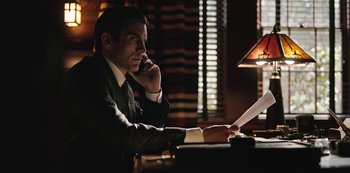 Movie still from “Yellowstone” (2018), created by John Linson – A man sitting at a table with a phone and a paper; Medium shot, Low angle