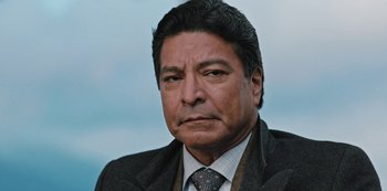 Movie still from “Yellowstone” (2018), created by John Linson – A man in a suit and tie looking at the camera; Close Up shot, Low angle