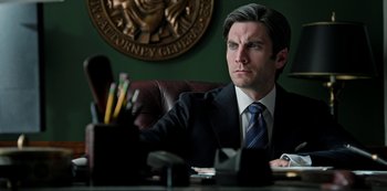 Movie still from “Yellowstone” (2018), created by John Linson – A man sitting at a desk in a suit; Close Up shot, Low angle