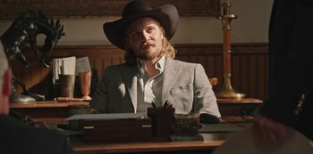 Movie still from “Yellowstone” (2018), created by John Linson – A man sitting at a table wearing a cowboy hat; Medium shot, Over the shoulder angle