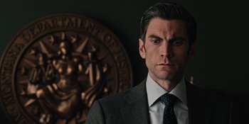 Movie still from “Yellowstone” (2018), created by John Linson – A man in a suit and tie standing in front of a seal; Close Up shot, Low angle