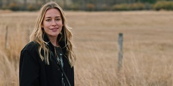 Movie still from “Yellowstone” (2018), created by John Linson – A woman standing in front of a dry grass field; Close Up shot, Over the shoulder angle